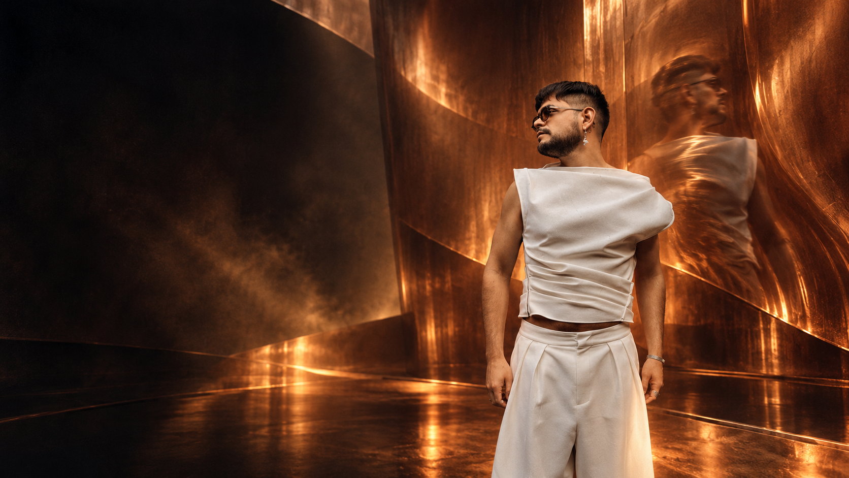 Manuex in sculptural ivory clothing amid glowing copper reflections and deep shadows.
